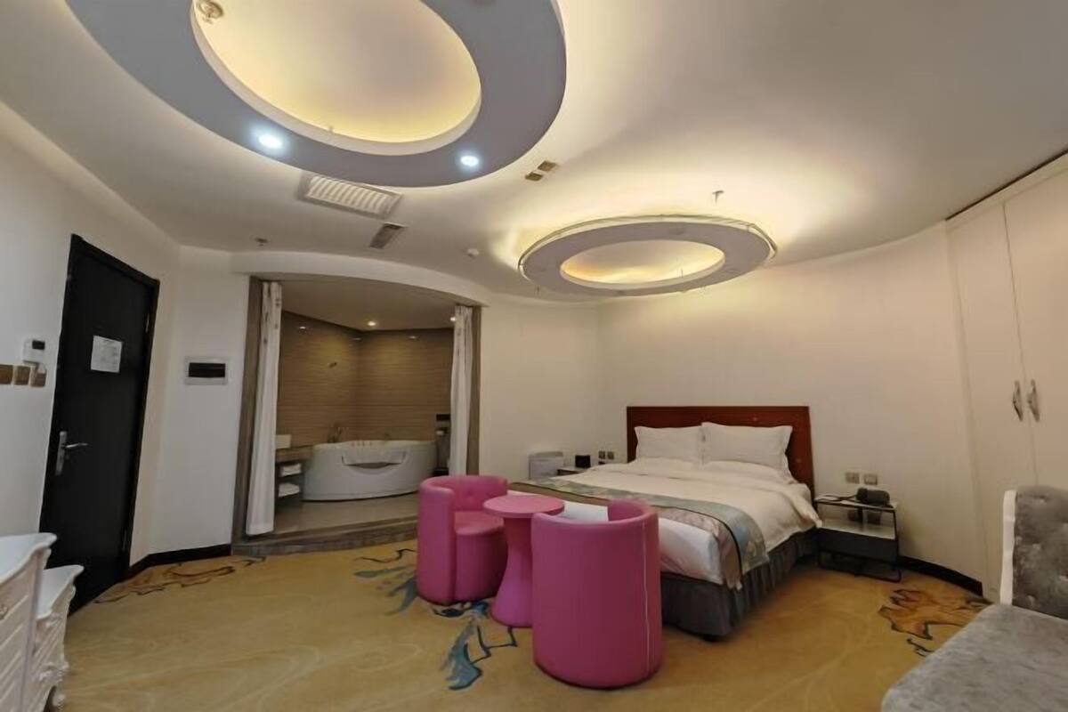 A modern hotel room with a bed, a vanity, a bathroom with a bathtub, and a circular ceiling light fixture.