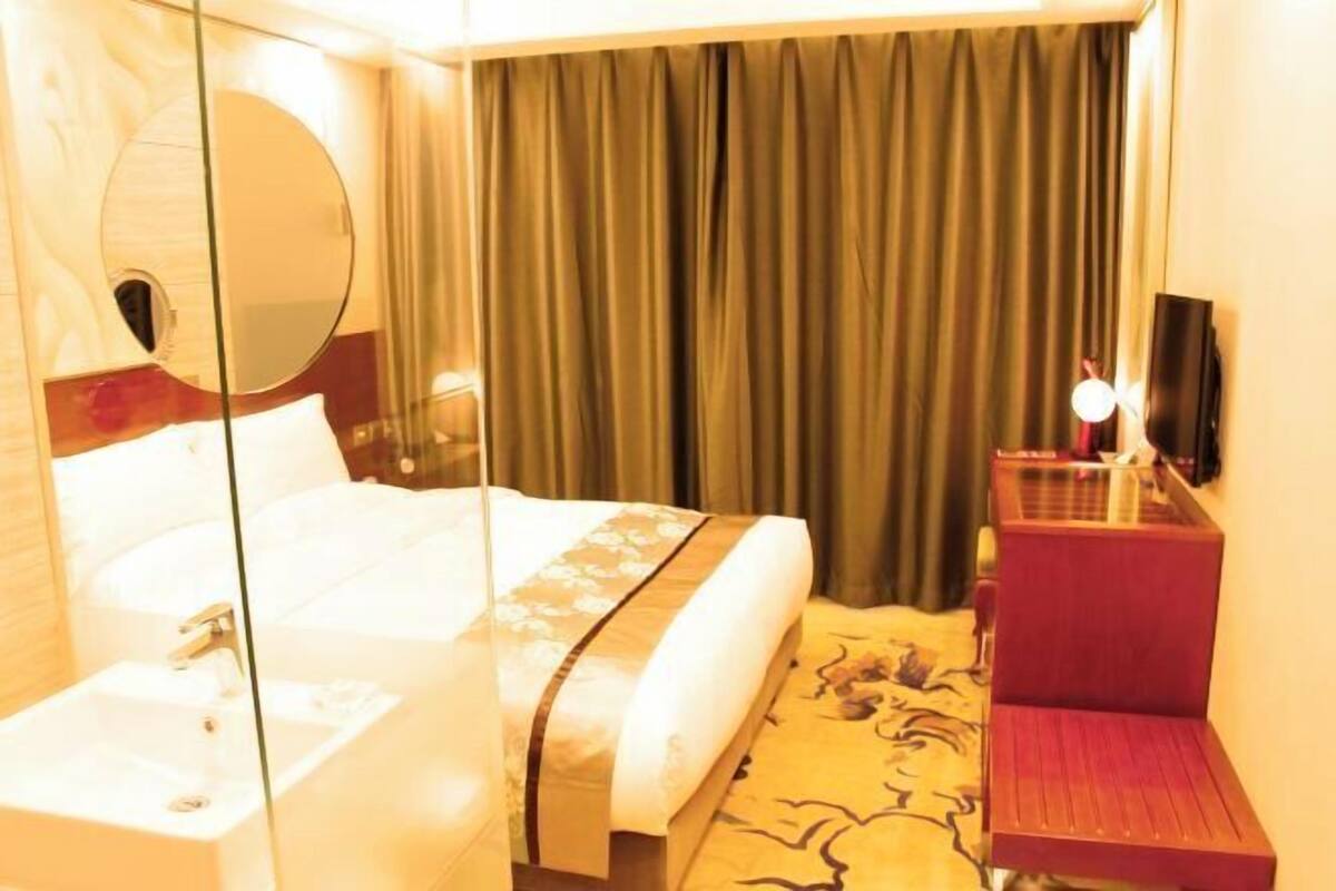 A hotel room with a bed, a bedside table, a mirror, a red chair, and a curtain.