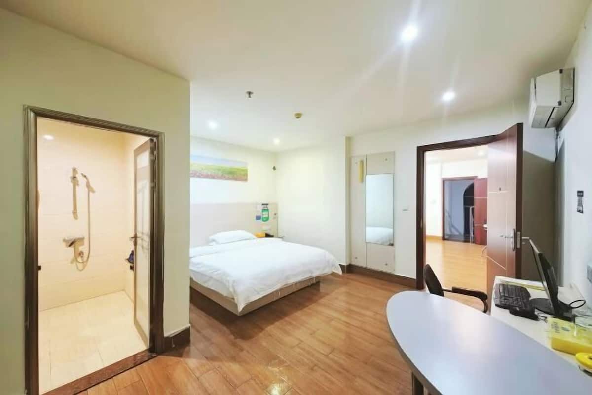 A hotel room with a bed, a desk with a computer, a shower, and a door leading to a hallway.
