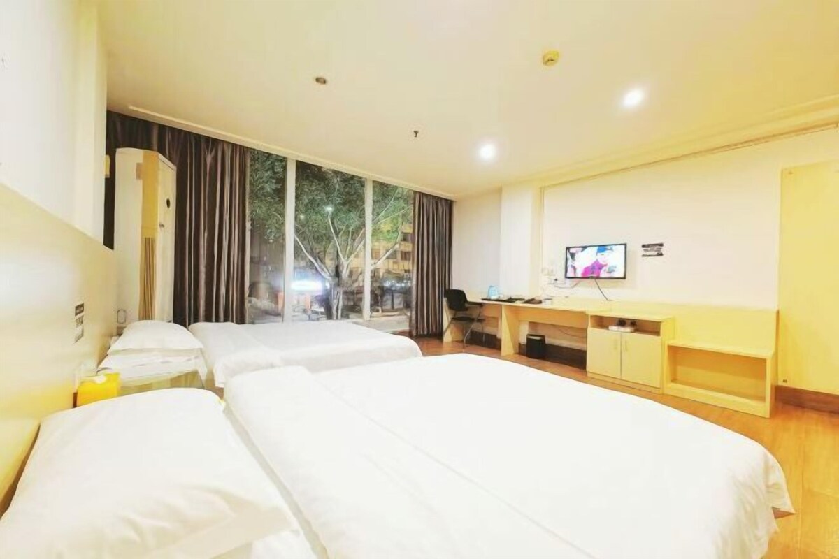 A hotel room with two beds, a desk, a TV, and a window with curtains.