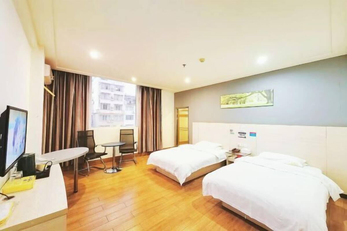 A hotel room with two beds, a desk, a chair, a TV, and a window with curtains.