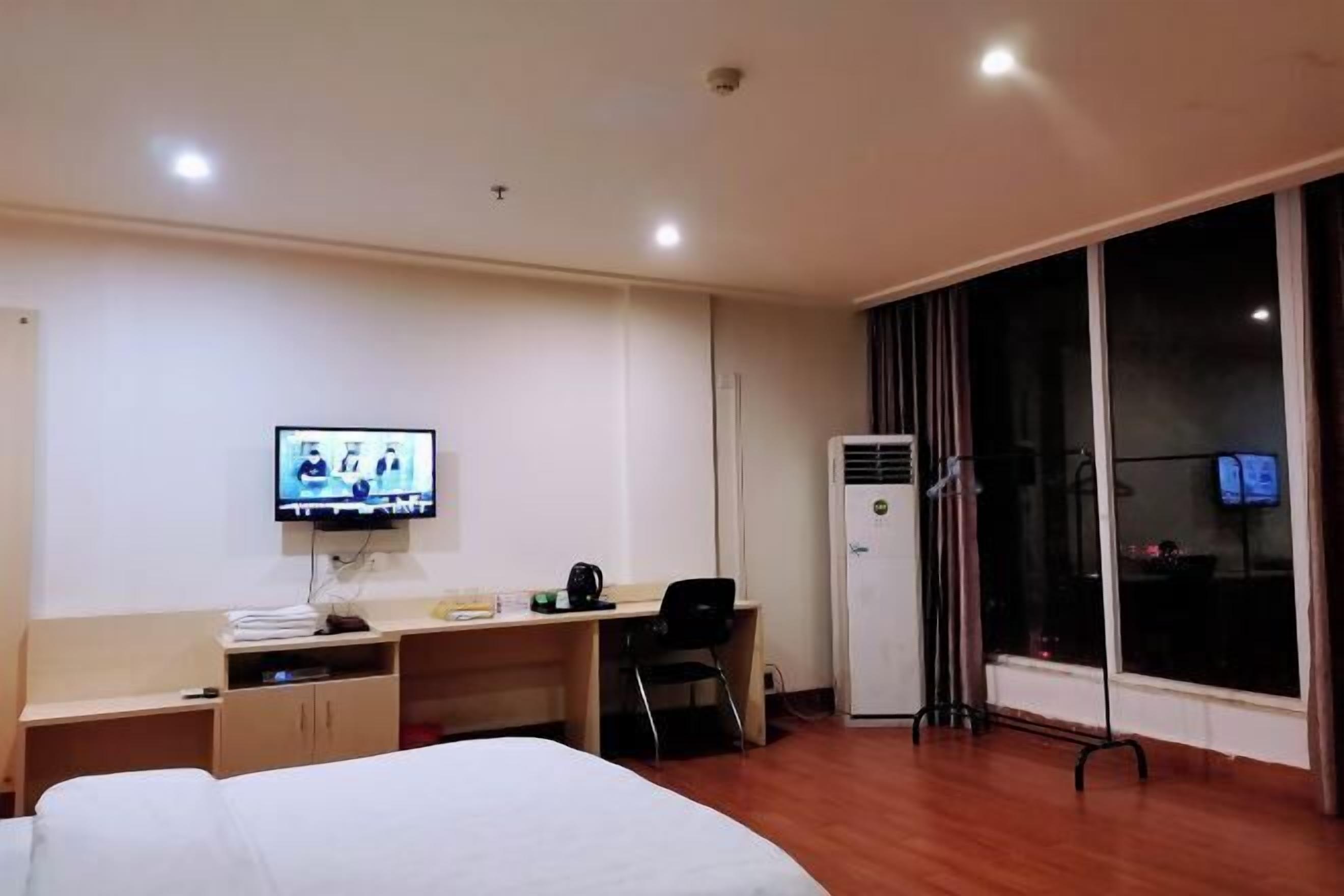 Habitación de hotel con cama, escritorio, televisión, aire acondicionado y ventana con cortinas.