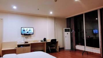 Habitación de hotel con cama, escritorio, televisión, aire acondicionado y ventana con cortinas.