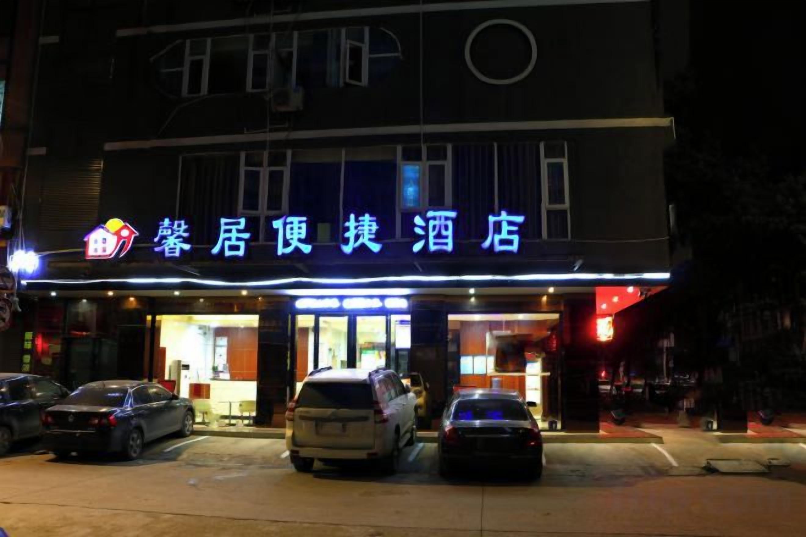 A hotel with a sign in a foreign language, multiple cars parked in front, and a well-lit entrance.