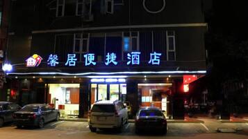 A hotel with a sign in a foreign language, multiple cars parked in front, and a well-lit entrance.