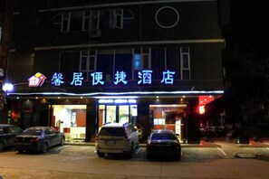 A hotel with a sign in a foreign language, multiple cars parked in front, and a well-lit entrance. - Xinju Express Hotel (Hezhou)