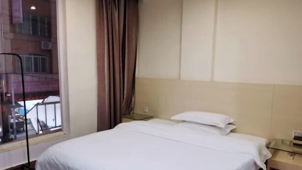 A hotel room with a bed, a nightstand, a window with curtains, and a view of the outside. - Xinju Express Hotel (Hezhou)