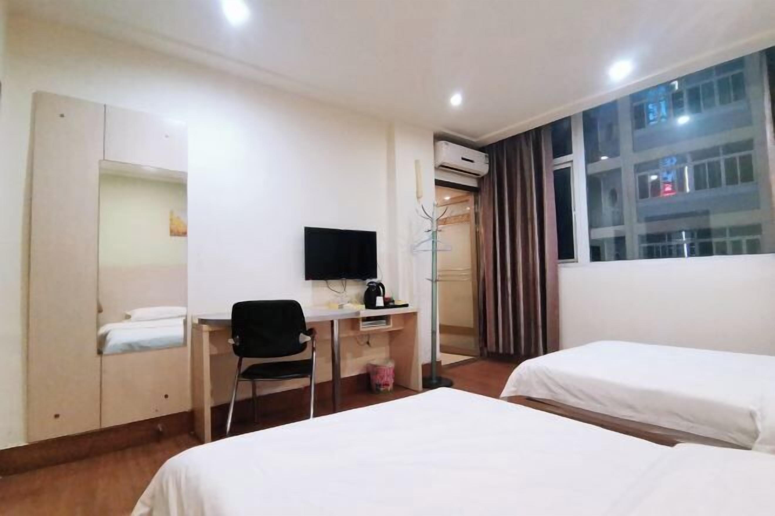 Habitación de hotel con dos camas, un escritorio con silla, un televisor y un equipo de aire acondicionado.