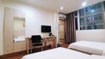 Habitación de hotel con dos camas, un escritorio con silla, un televisor y un equipo de aire acondicionado.