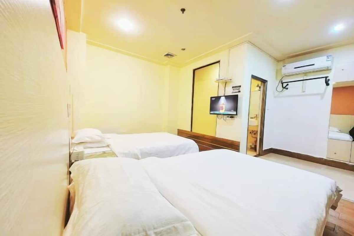 A hotel room with two beds, a television, an air conditioning unit, and a small bathroom.