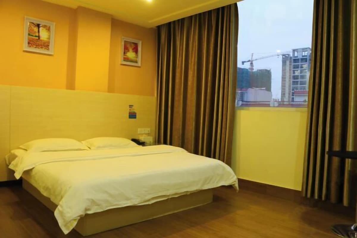 A hotel room with a bed, two paintings on the wall, and a view of construction outside.