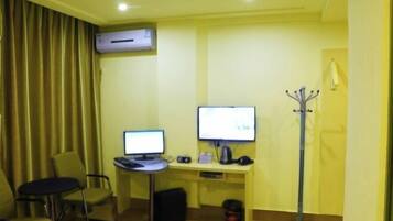 A hotel room with two desks, two computers, a coat rack, and a window with curtains.