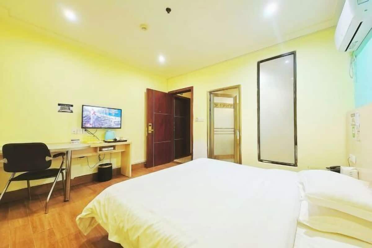 A hotel room with a bed, a desk with a computer, a chair, and a wardrobe.
