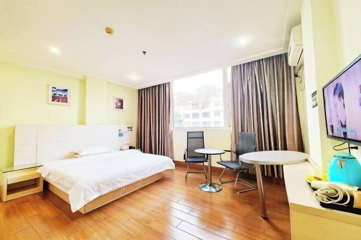 A hotel room with a bed, a desk, a chair, a TV, and a window with curtains.