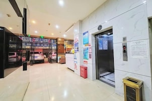 Um saguão de hotel com balcão de recepção, elevador e entrada por porta de vidro.