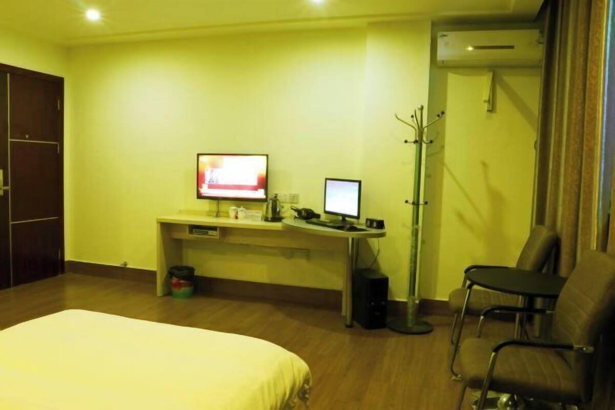 A hotel room with a bed, a desk with a computer, a chair, and a coat rack.