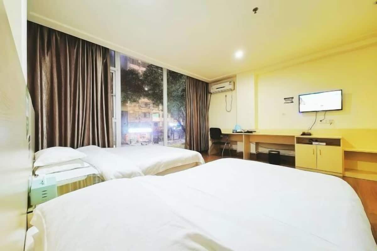 A hotel room with two beds, a desk, a television, and an air conditioning unit.