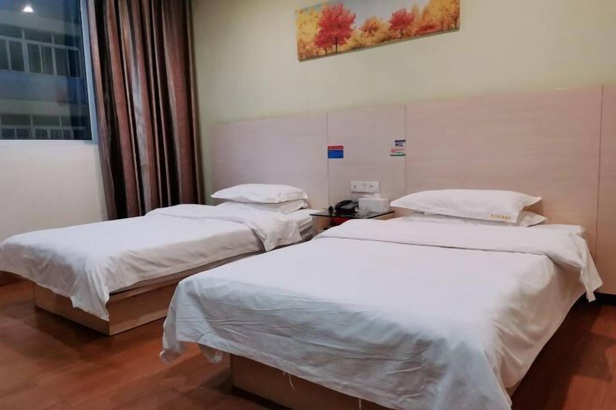 A hotel room with two single beds, a window with curtains, a painting on the wall, and a wooden floor.