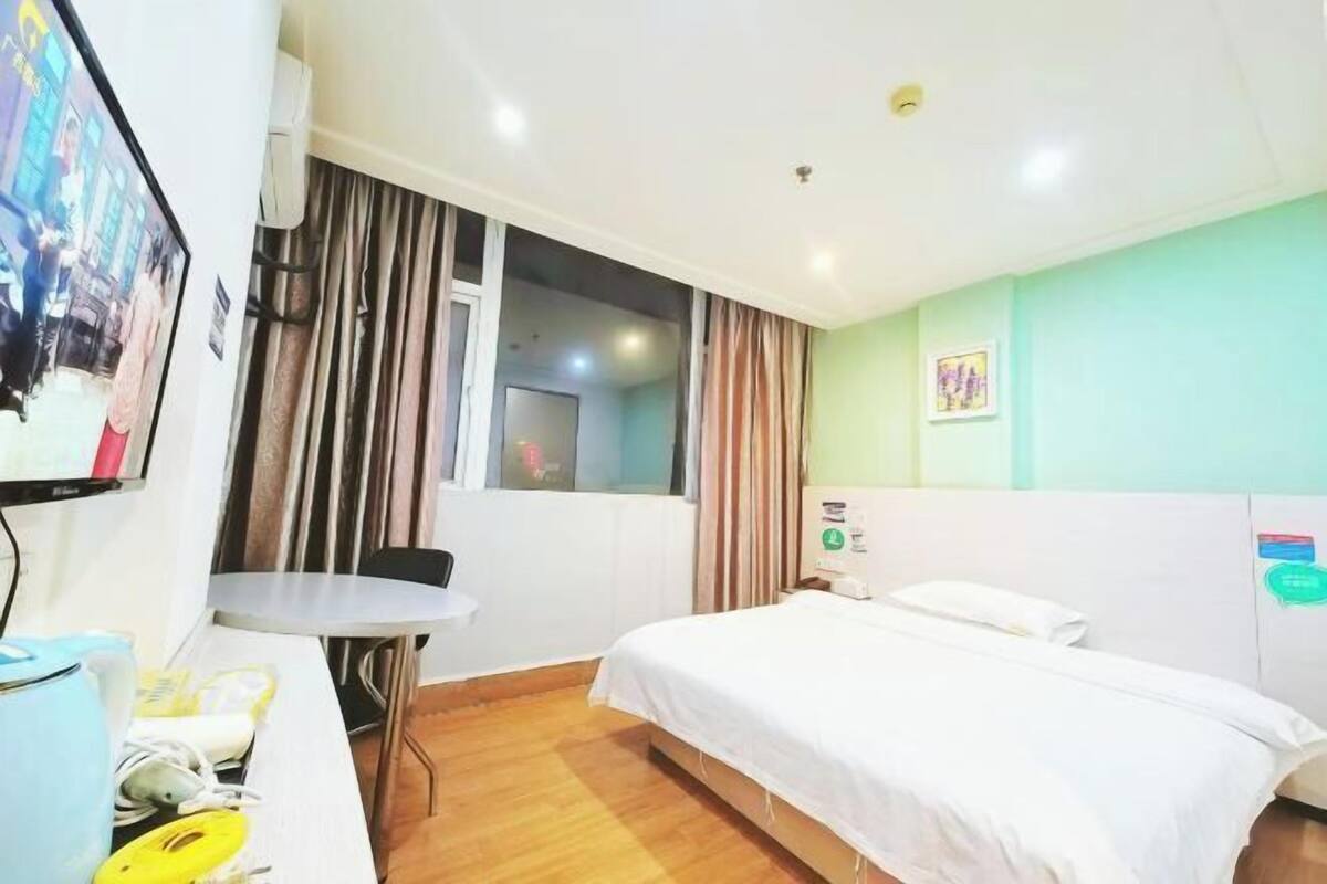 A hotel room with a bed, a desk with a chair, a television, and a window with curtains.