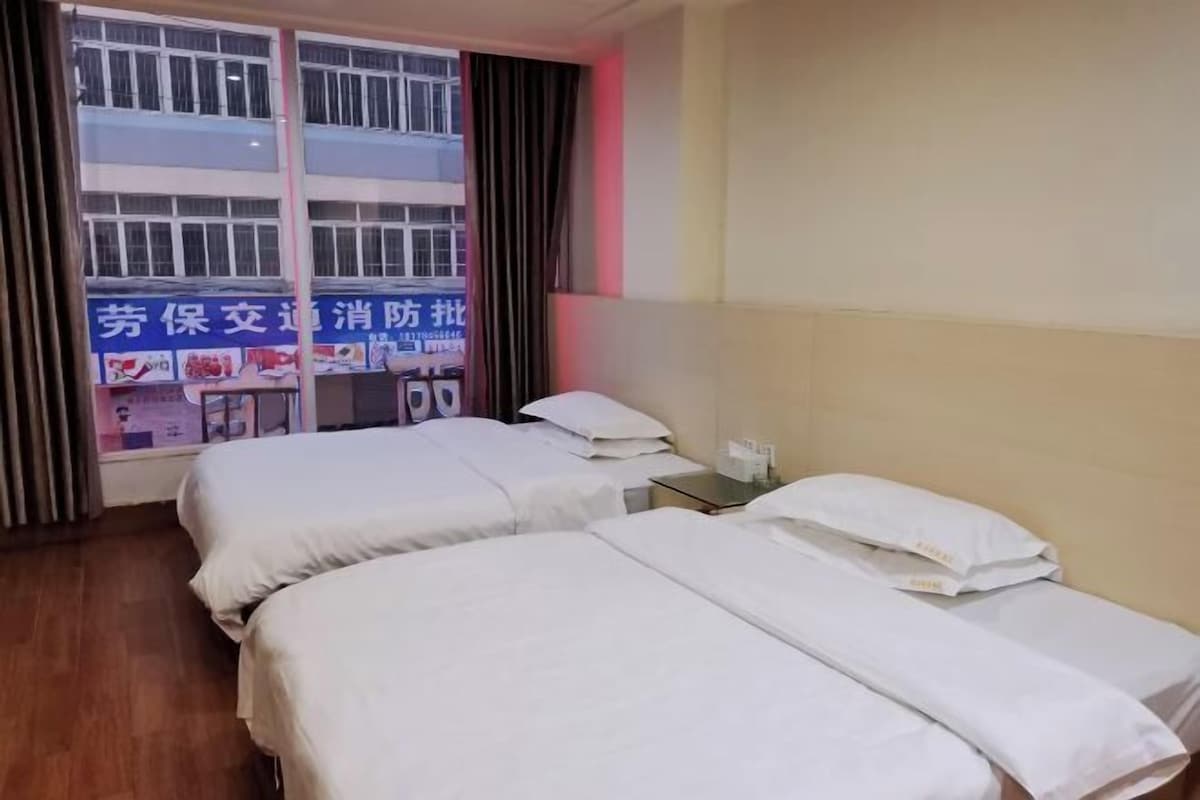 A hotel room with two beds, a window with curtains, a bedside table, and a wall with a sign.