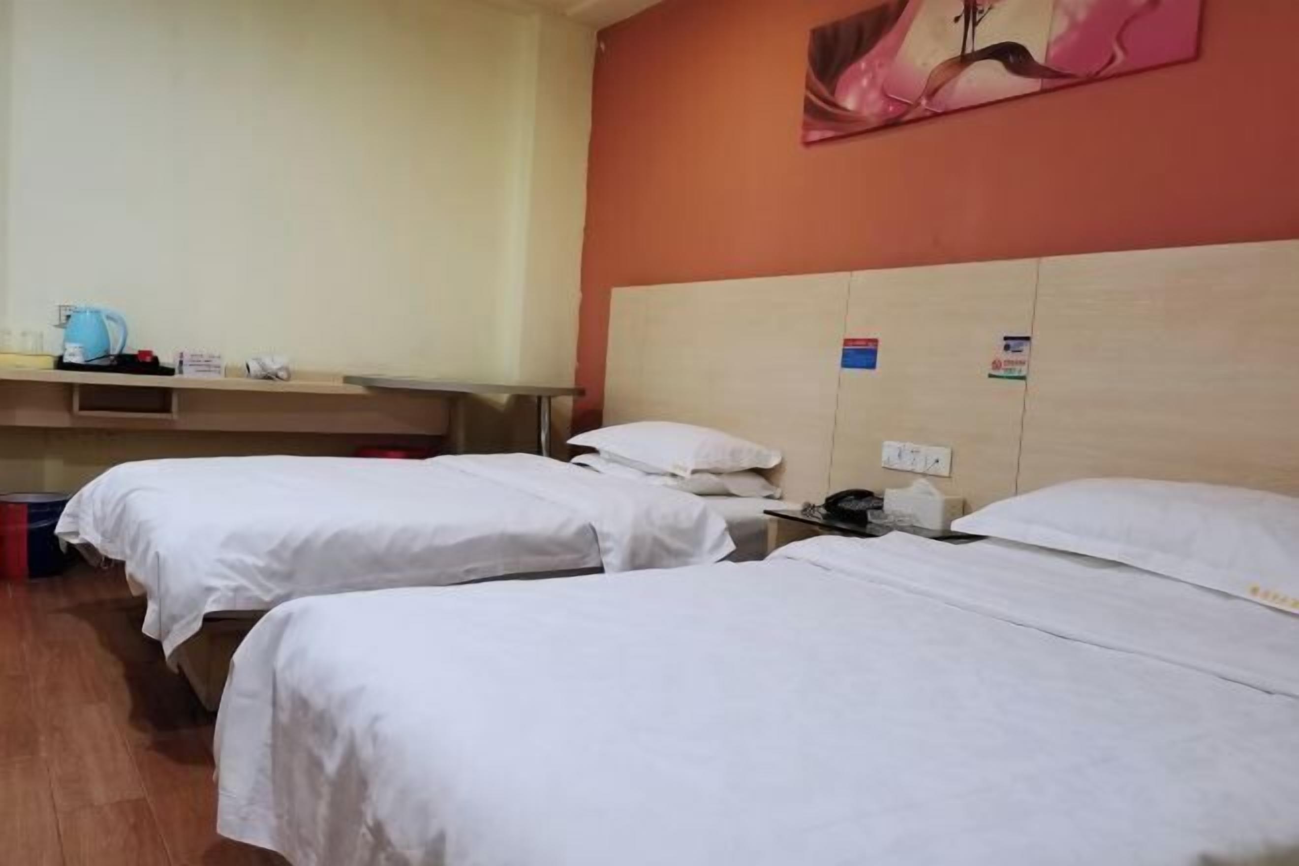 A hotel room with two single beds, a wooden floor, a small table with a kettle, and a painting on the wall.