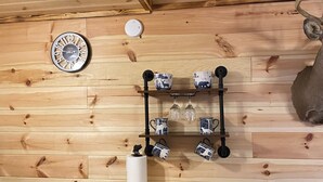 Ein Holzinnenraum mit Holztisch, einem Stuhl, einer Uhr und einem Regal mit Tassen und Gläsern.