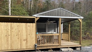 Eine Holzhütte mit Veranda, Deckenventilator und Fenster mit Blick auf einen bewaldeten Bereich.