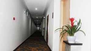 A hotel hallway with a patterned carpet, a potted plant, and a fire alarm on the wall. - Lihuang Hotel (Jiaxing)
