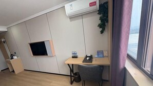 A room with a desk, chair, mounted TV, air conditioning unit, and a window with a view. - Lihuang Hotel (Jiaxing)