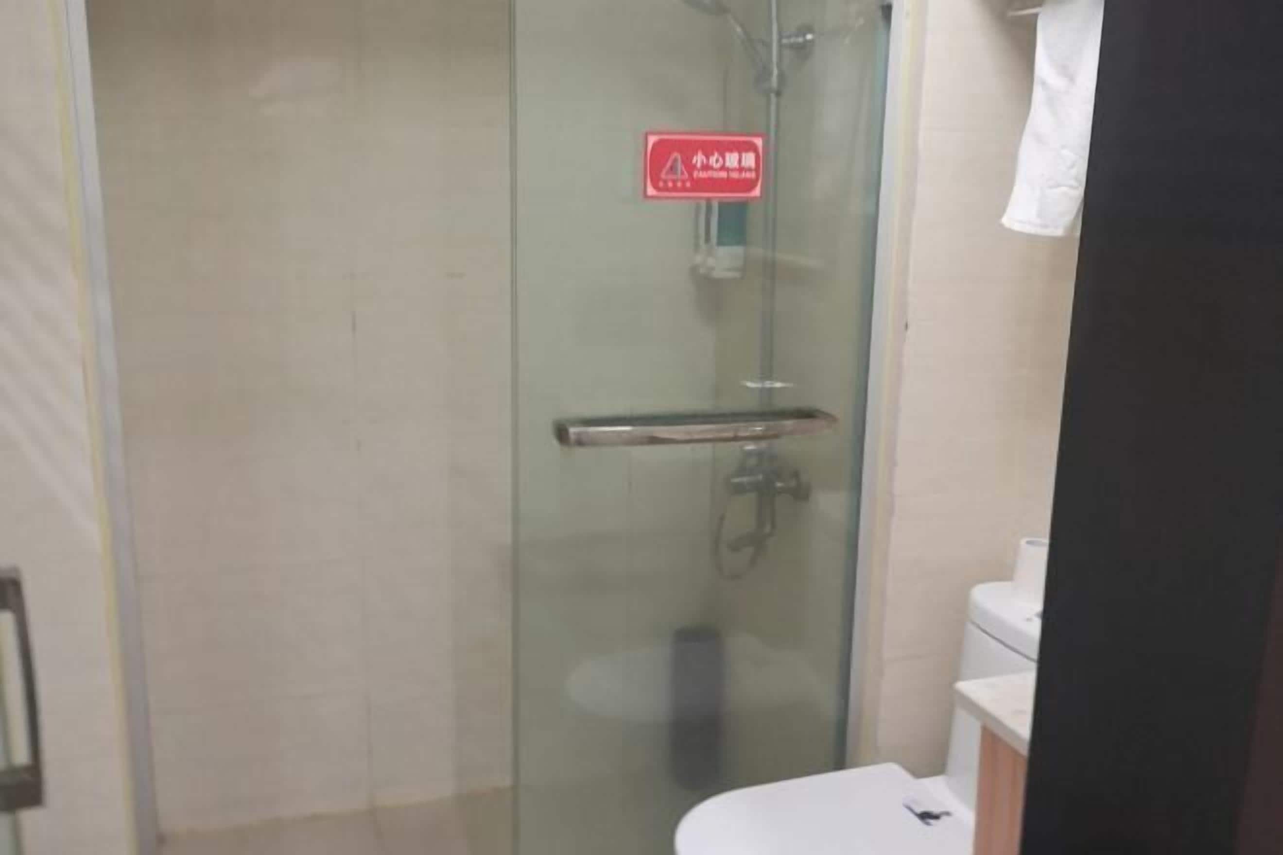 Een douchecabine met glazen wanden, een rood veiligheidsteken, een wit toilet en een witte wastafel.