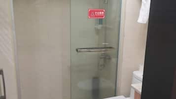 Een douchecabine met glazen wanden, een rood veiligheidsteken, een wit toilet en een witte wastafel.