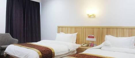 A hotel room with two beds, a wooden headboard, a bedside table with a phone, and a chair.