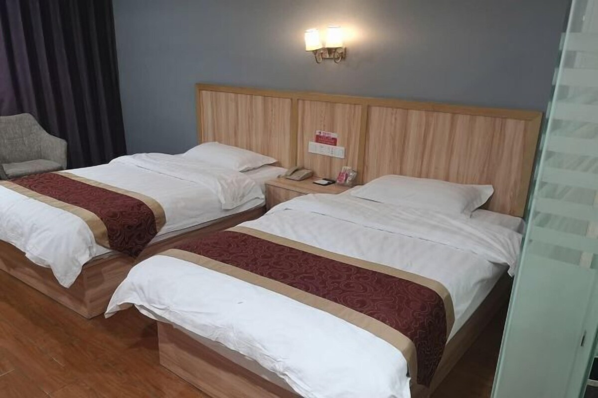 A hotel room with two beds, a wooden headboard, a bedside table with a phone and a lamp, and a chair.