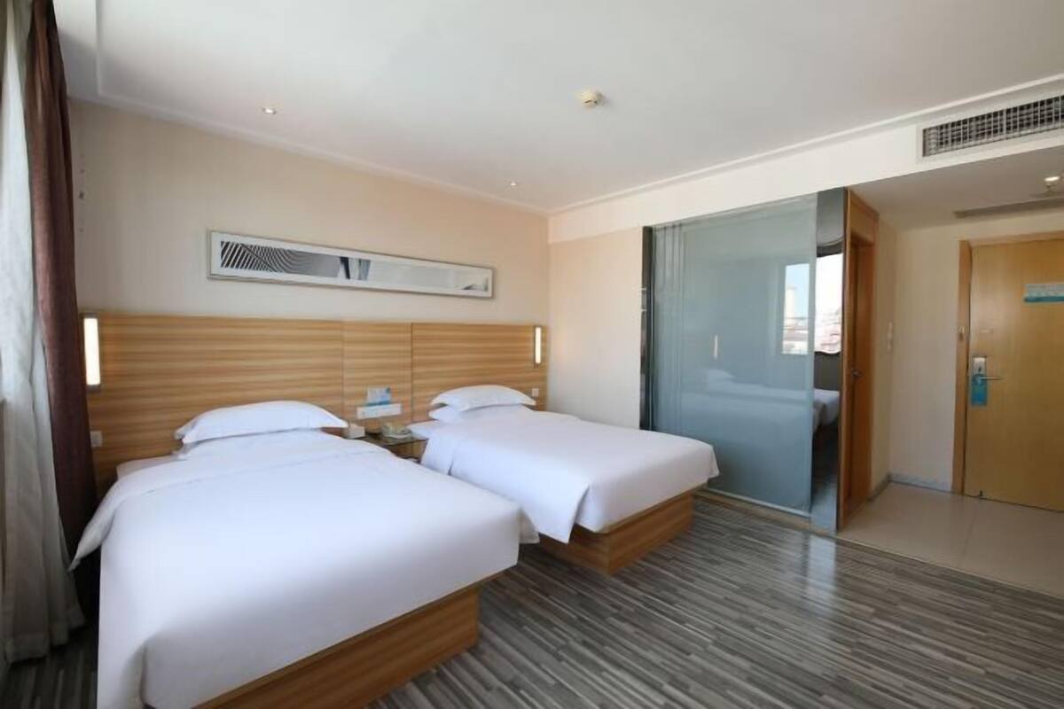 Ein Hotelzimmer mit zwei Betten, einem Holzkopfstück, einem Nachttisch und einem großen Fenster.