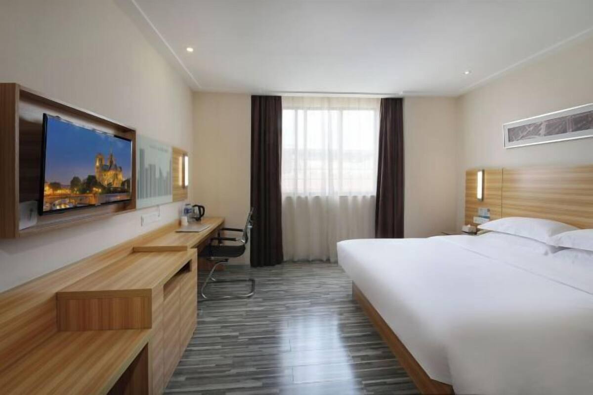 Ein Hotelzimmer mit Bett, Schreibtisch, Stuhl, Wandfernseher und einem Fenster mit Vorhängen.