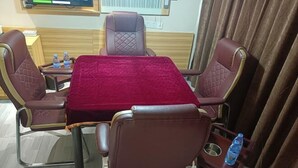 A hotel room with a rectangular table covered with a red cloth, surrounded by four brown leather chairs with armrests. There are two bottles of water on the table and a small tray with a water bottle on the side. - Mingji Hotel (Guangzhou Shawan Old Town) (Guangzhou)