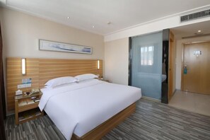 Ein Hotelzimmer mit einem großen Bett, einem Holzkopfschild, einem Nachttisch mit Lampe und einem Bild an der Wand.