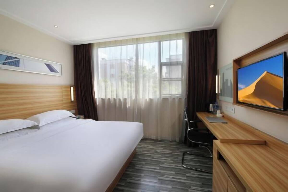 Ein Hotelzimmer mit einem großen Bett, einem Schreibtisch, einem Stuhl und einem Fernseher an der Wand.