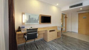 A hotel room with a wooden desk, a black chair, a flat-screen TV mounted on the wall, and a small plant on the desk. - Mingji Hotel (Guangzhou Shawan Old Town) (Guangzhou)