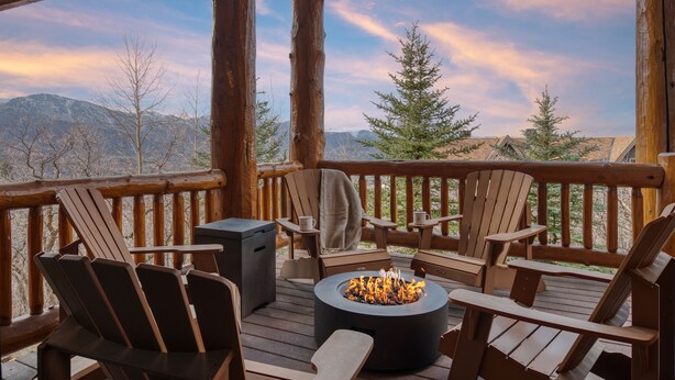 Une terrasse en bois avec des fauteuils Adirondack, un foyer et une vue sur les montagnes.