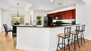 Een moderne keuken met een centraal eiland, donkere houten kastjes en een eethoek met stoelen.