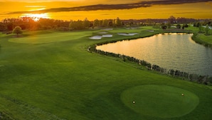 Een golfbaan met een vijver, bomen en een zonsondergang.