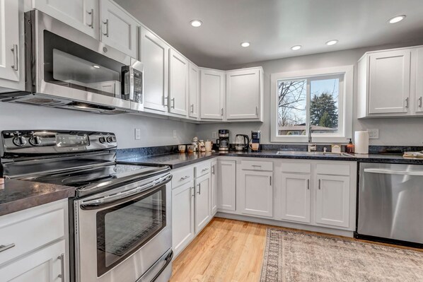 A modern kitchen with stainless steel appliances, white cabinetry, and a large window providing natural light.