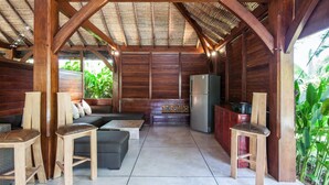 Ein überdachter Außenbereich mit Holzmöbeln, einer Couch und einem Kühlschrank.