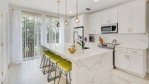 Una cocina moderna con armarios blancos, una isla grande con taburetes de bar, un microondas y una estufa.