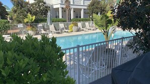 A pool area with lounge chairs and a white fence.