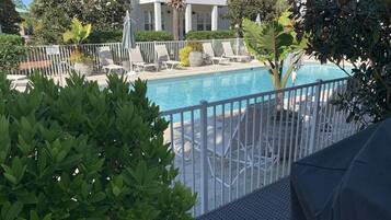 A pool area with lounge chairs and a white fence.