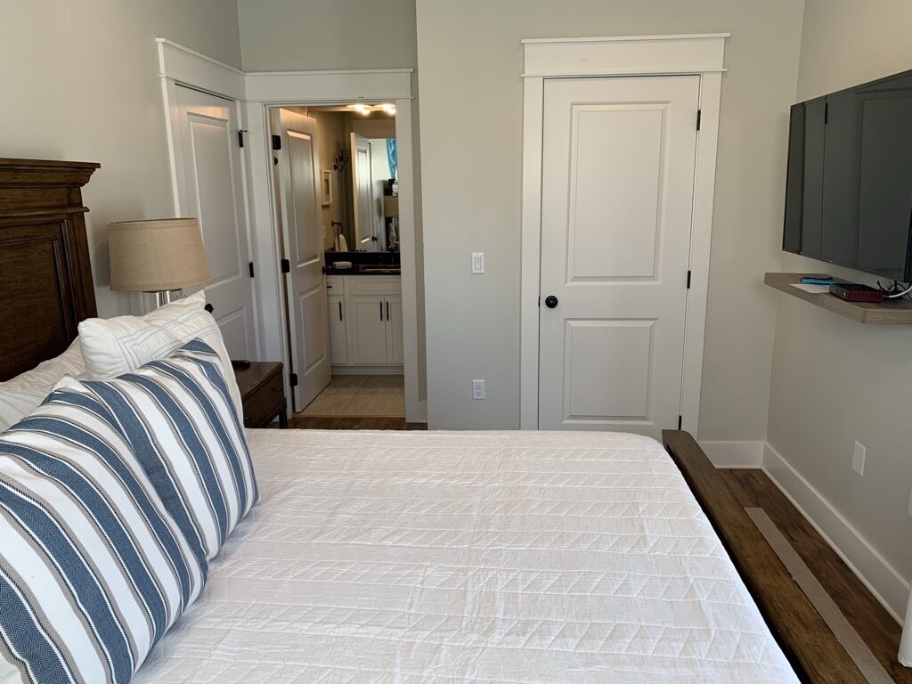 A bedroom with a bed, a nightstand, a lamp, a TV, and a door leading to a bathroom.