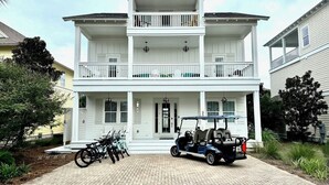 A two-story white house with a balcony, a driveway, and a golf cart parked in front.