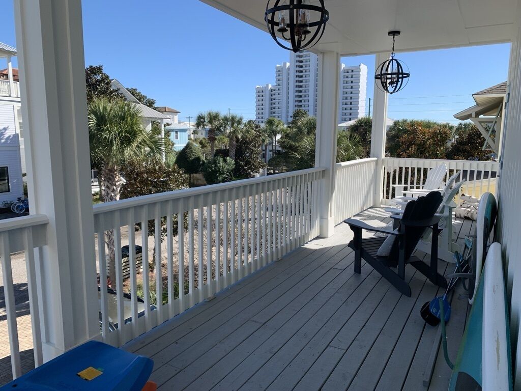 A covered outdoor deck with a white railing, a table with chairs, and a hanging light fixture.